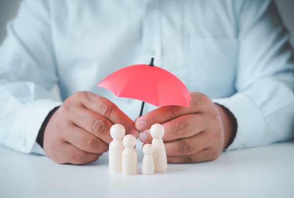 business man holding a red umbrella over figurines in the shape of people