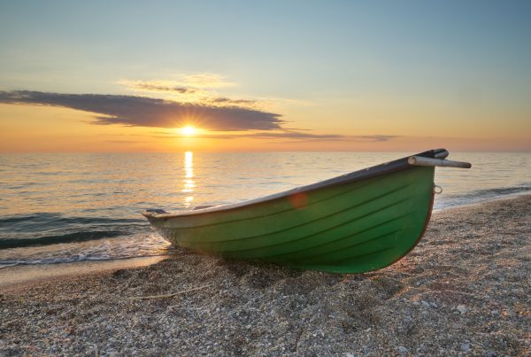 Green fishing boat on the seashore at sunset. Nature scene.